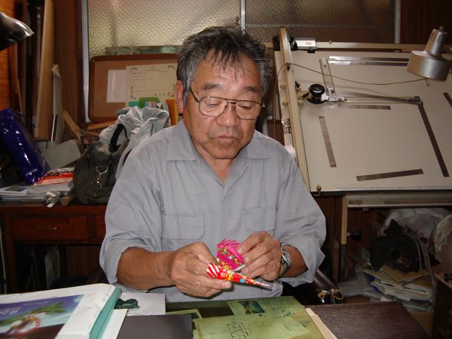 不二家のパラソルチョコを手に、当時、自分が作ったパラソル巻き機のことを説明する池田社長。